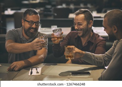 Cheerful Smiling Men Holding Glasses With Alcohol Beverages And Laughing. Three Friends Spending Time Together And Having Fun In Bar. Men Drinking Scotch, Whiskey Or Brandy.