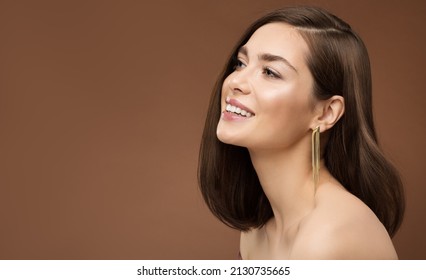 Cheerful Smiling Model Profile Side View. Brunette Beauty Woman with Nude Make up Smooth Skin and Golden Earring over Brown Background