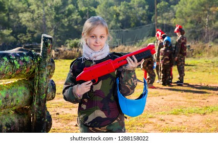 Cheerful  Smiling Teen Girl Wearing Uniform And Holding Gun Ready For Playing With Friends On Paintball Outdoor