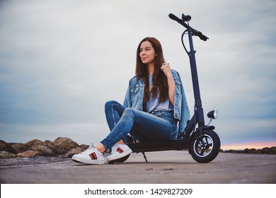 Cheerful smiling woman is chilling on her new electro scooter at seaside in cloudy day. - Powered by Shutterstock