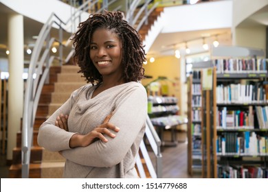 Cheerful smiling woman posing at public library. Front view of smiling lady with dreadlocks posing in front of stairs. Knowledge concept