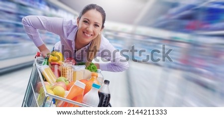 Cheerful smiling woman pushing a trolley at the supermarket, offers and sales concept