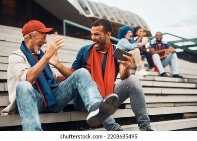 Cheerful sports fan and his senior father celebrating while watching soccer match on smart phone outdoors. - Powered by Shutterstock