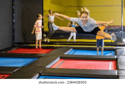 Cheerful sporty preteen girl having fun in indoor amusement park, doing side splits in air while bouncing on trampoline.. - Powered by Shutterstock