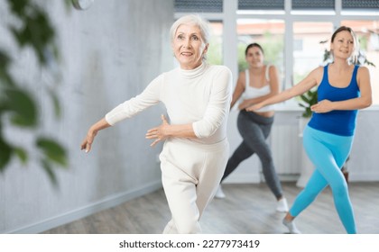 Cheerful sporty senior woman training movements of rhythmic dance with group in fitness studio. Concept of active lifestyle of aged adults - Powered by Shutterstock