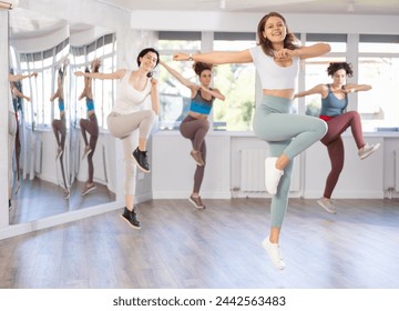 Cheerful sporty young girl captured in air while jumping during lively dance fitness routine with group of women in studio - Powered by Shutterstock