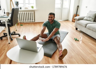 Cheerful Stretching. Male Fitness Instructor Showing Exercises While Streaming, Broadcasting Video Lesson On Training At Home Using Laptop. Sport, Online Gym Concept. Horizontal Shot