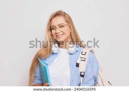 Cheerful student posing with paper folder and backpack smiling while standing isolated on studio backfrop, good day concept, copy space.