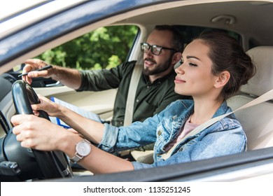 cheerful student and teacher in car at driving test 