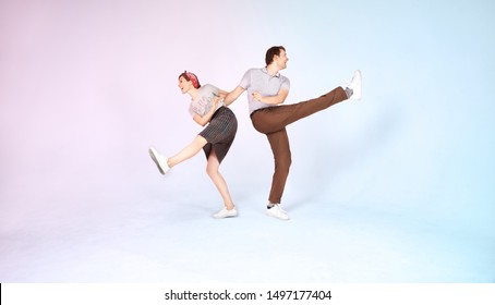 Cheerful stylish couple is dancing vintage joyful jazz dance called lindy hop indoors in the studio on colored background