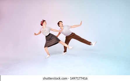Cheerful stylish couple is dancing vintage joyful jazz dance called lindy hop indoors in the studio on colored background