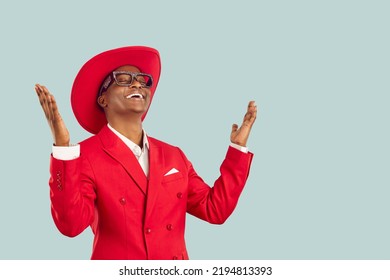 Cheerful Stylish And Inspired Happy Dark-skinned Man Who Thanks With Relief By Raising His Hands And Smiling Broadly. Man In Red Fashion Outfit Enjoys With Closed Eyes On Pastel Light Blue