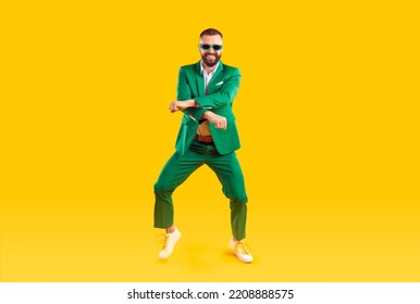 Cheerful and stylish man is having fun dancing in Gangnam style at St. Patrick's Day party. Young man in trendy youth green suit and sunglasses is dancing and laughing on orange background. Banner.
