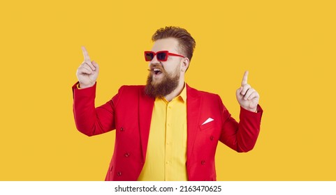 Cheerful And Stylish Young Extravagant Chubby Man Having Fun And Dancing On Yellow Background. Funny Bearded Red-haired Guy Partygoer In Red Jacket And Sunglasses Is Having Fun. Banner.