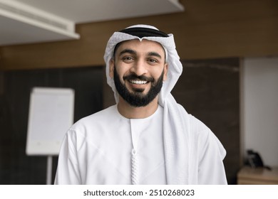 Cheerful successful Arab business leader man wearing keffiyeh, looking at camera, smiling, speaking on video call with office white board in background. Happy Arabic businessman head shot portrait - Powered by Shutterstock