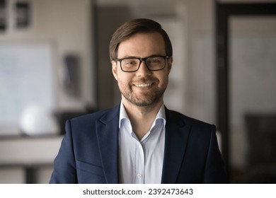 Cheerful successful business professional man in stylish eyeglasses and office suit looking at camera, smiling, posing for professional portrait. Confident boss, business leader video call head shot - Powered by Shutterstock