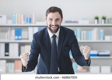 Cheerful Successful Businessman Smiling In His Office With Raised Fists, Winning And Enthusiasm Concept