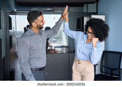 Cheerful successful coworkers colleagues indian businessman and African American businesswoman giving high five celebrating project victory in modern office. Business corporate culture concept.