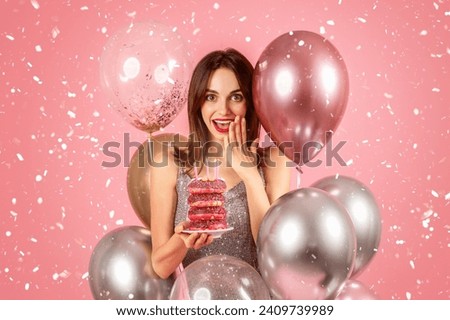 Cheerful surprised millennial caucasian woman in dress with many balloons hold cake with donuts, isolated on pink background, studio. Ad and offer, celebration holiday, birthday party with confetti