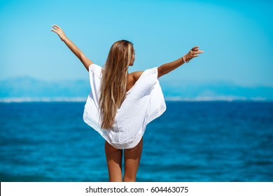 Cheerful tanned woman in bikini at beach enjoying nature-freedom. Perfect body model outdoors at tropical resort with her arms outstretched the wind. Beautiful young female enjoying day at ocean beach