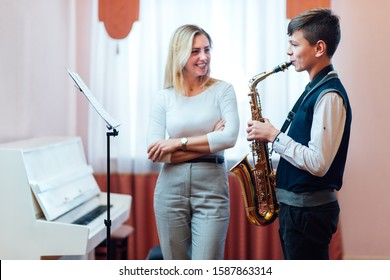 Cheerful Teacher With Student Boy Learning Saxophone Lessons At Music School