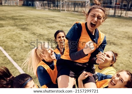 Cheerful team of female soccer players celebrating victory and carrying on of teammates who is shouting out of joy on stadium.