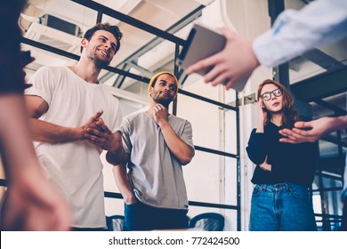 Cheerful Team Members Discussing Project Planning Using Touchpad For Searching Information Online, Crew Of Creative Designers Sharing Ideas And Opinions During Brainstorming Session In Office