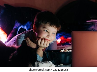 Cheerful Teen Boy Using Laptop At Home Watching Funny Movie Cartoon Eat Pop Corn, Browsing Internet On Sofa In Living Room. Smiling Kid Looking At Screen Having Fun Enjoying Weekend Night Vacation.