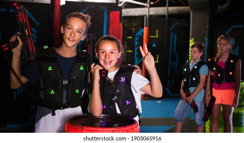 Cheerful teen girl and boy with laser pistols posing together in laser tag labyrinth..