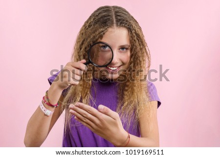 Cheerful teen girl with long blond curly hair looking through a magnifying glass.