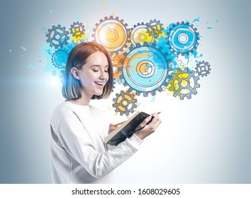 Cheerful teen girl and notebook   pen standing near gray wall and colorful gears sketch drawn it  Concept brainstorming   education 