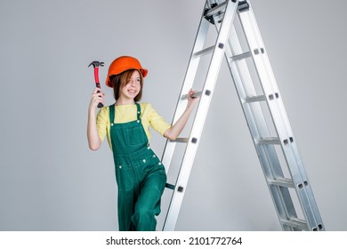 Cheerful Teen Girl In Working Uniform And Helmet On Ladder Use Hammer, Fix