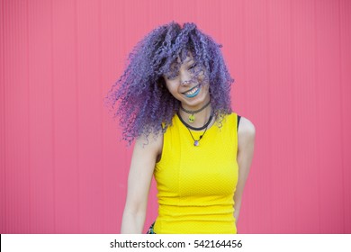 Cheerful Teen Woman With Purple Afro Hair And Blue Lips On A Pink Wall