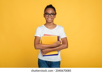 Cheerful Teenage African American Girl Pupil In Glasses And Casual Holds Books And Ready To Learn, Isolated On Yellow Background, Free Space. Modern Education, Knowledge, Back To School In Autumn