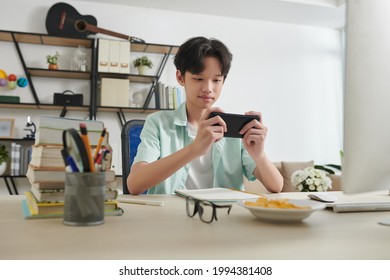 Cheerful teenage boy playing game on smartphone instead of doing homework at home - Powered by Shutterstock