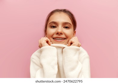 cheerful teenage girl with braces holds a warm soft white sweater on a pink isolated background, child rejoices in warm winter knitted clothes - Powered by Shutterstock