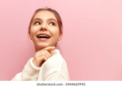 cheerful teenage girl with braces smiles and looks away on a pink isolated background, child looks at copy space - Powered by Shutterstock