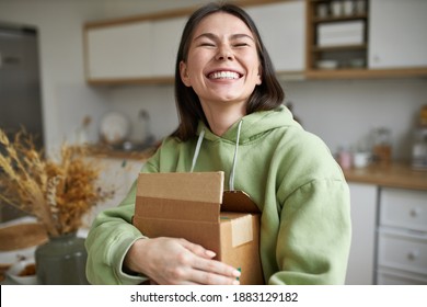 Cheerful teenage girl expressing positive emotions receiving unexpected birthday gift holding parcel and smiling with pleasure. Dark haired young woman posing with cardboard box with new cosmetics