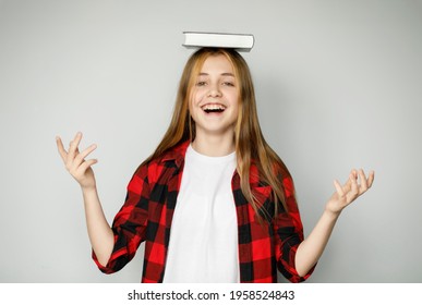 Cheerful teenage girl holding a book on her head, the joy of education. Enjoy learning.