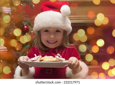 Cheerful toddler girl in hat holding plate with cookies and candy for santa claus - Powered by Shutterstock