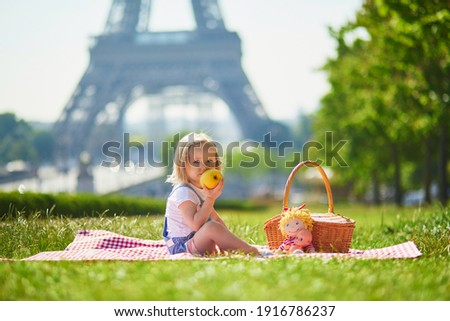 Cheerful toddler girl having picnic near the Eiffel tower in Paris, France. Happy child playing with toys in park on a summer day. Kid enjoying healthy snacks outdoors