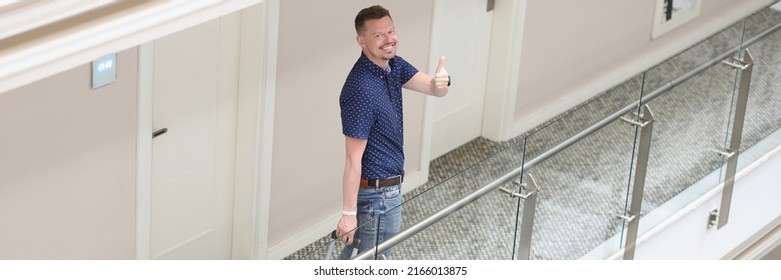 Cheerful tourist man with suitcase search for his room in hotel show thumbs up gesture