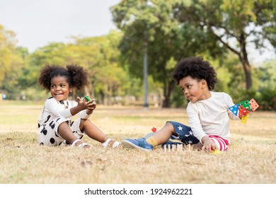 Cheerful Two African American Little Boy And Girl Playing Toy Together In The Park. Children With Curly Hair Having Fun Together Outdoor. Black Kid People Enjoying Outside