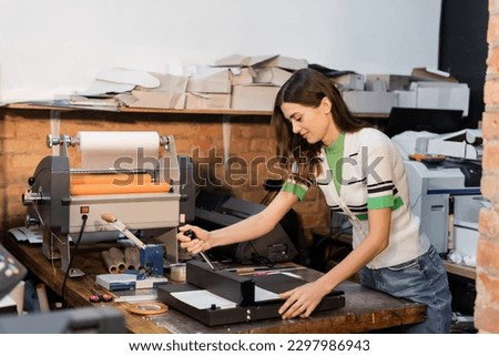 cheerful typographer using paper trimmer next to print plotter in print center