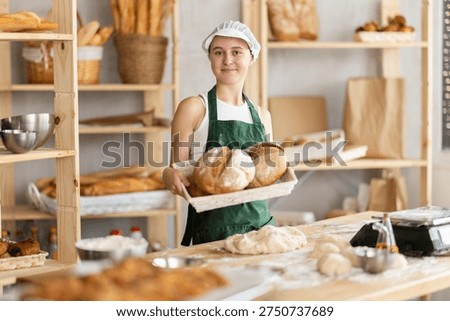 Cheerful underage girl demonstrating bread in right-angled woven basket in bakehouse