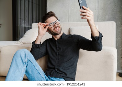 Cheerful Unshaven Man Taking Selfie On Smartphone While Sitting On Floor At Home