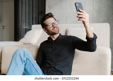 Cheerful Unshaven Man Taking Selfie On Smartphone While Sitting On Floor At Home