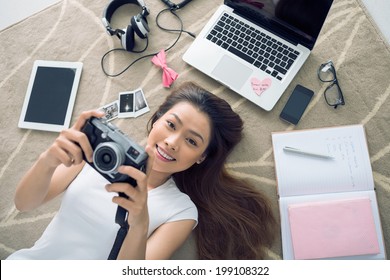 Cheerful Vietnamese girl lying on the floor  with her camera in hands - Powered by Shutterstock