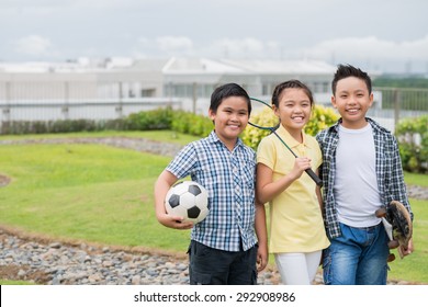 Cheerful Vietnamese kids with sports equipment standing outdoors