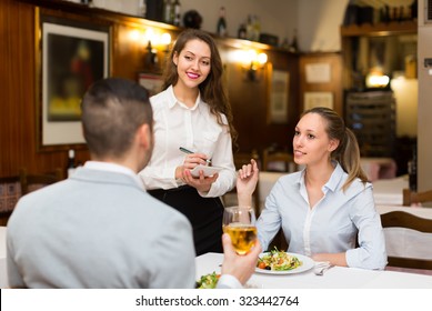 Cheerful waitress offering to young couple tasty dishes. Focus on girl  